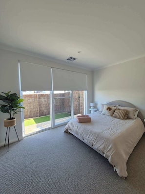 Une chambre à coucher avec un lit, une plante en pot, une porte-fenêtre coulissante et une vue sur une cour clôturée.