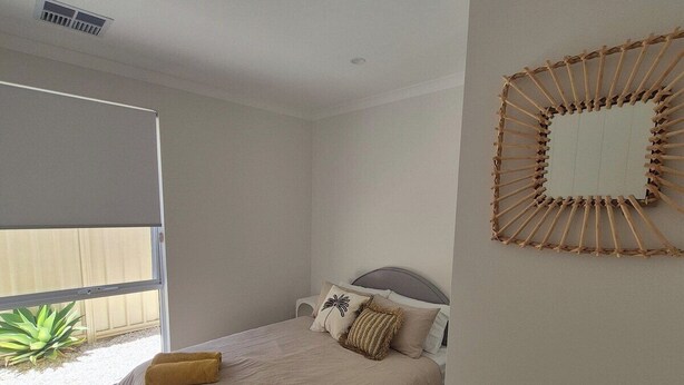 A bedroom with a bed, a window, a ceiling vent, and a wall-mounted mirror.
