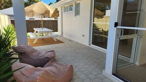 Um pátio com mesa e cadeiras, área de estar coberta e porta de vidro que dá para um espaço exterior coberto.