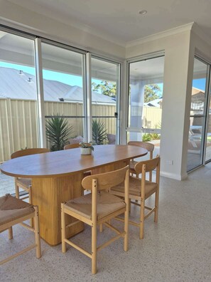 A modern dining area with a round wooden table and matching chairs, large glass doors leading to a backyard, and a view of a residential area.