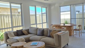 A spacious living room with a large sectional sofa, two round wicker coffee tables, and a dining area with a wooden table and chairs.