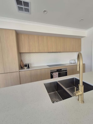A modern kitchen with wooden cabinets, stainless steel appliances, and a gold faucet.