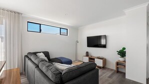 Een moderne woonkamer met een hoekbank, een flatscreen televisie, een bijzettafeltje en een plant in pot.