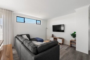A modern living room with a sectional sofa, a flat-screen TV, a small side table, and a potted plant.