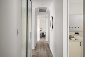 Un couloir avec un plancher en bois, une porte en verre, un mur blanc et une salle de bain avec un lavabo et un miroir.