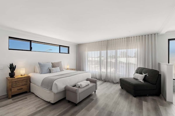 A modern bedroom with a bed, a sofa, a nightstand, and a window.