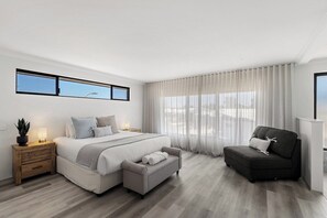 A modern bedroom with a bed, bedside tables, a sofa, and a window.
