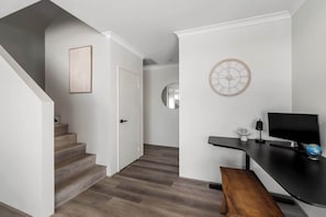 Un intérieur moderne avec un escalier, un bureau doté d’un ordinateur et une horloge murale ronde.
