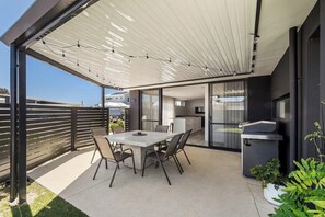 An outdoor patio with a dining table and chairs, a grill, and a covered area with string lights.