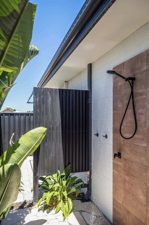 Un espace de douche extérieur moderne, doté d’une porte en bois, d’un pommeau de douche en métal et d’un tuyau noir.