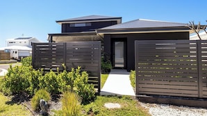 Een modern huis met een donkere gevel, een duidelijke inkom en een pad dat naar de deur leidt.