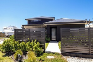 A modern house with a dark exterior, a visible entrance, and a pathway leading to the door.