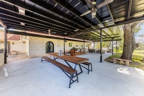 An outdoor patio with a long wooden table and benches, surrounded by chairs and a small bar area. - Spacious 90-acre Ranch Ideal for Families Reunions Events Sleeps 13 San Marcos River Access (Gonzales)