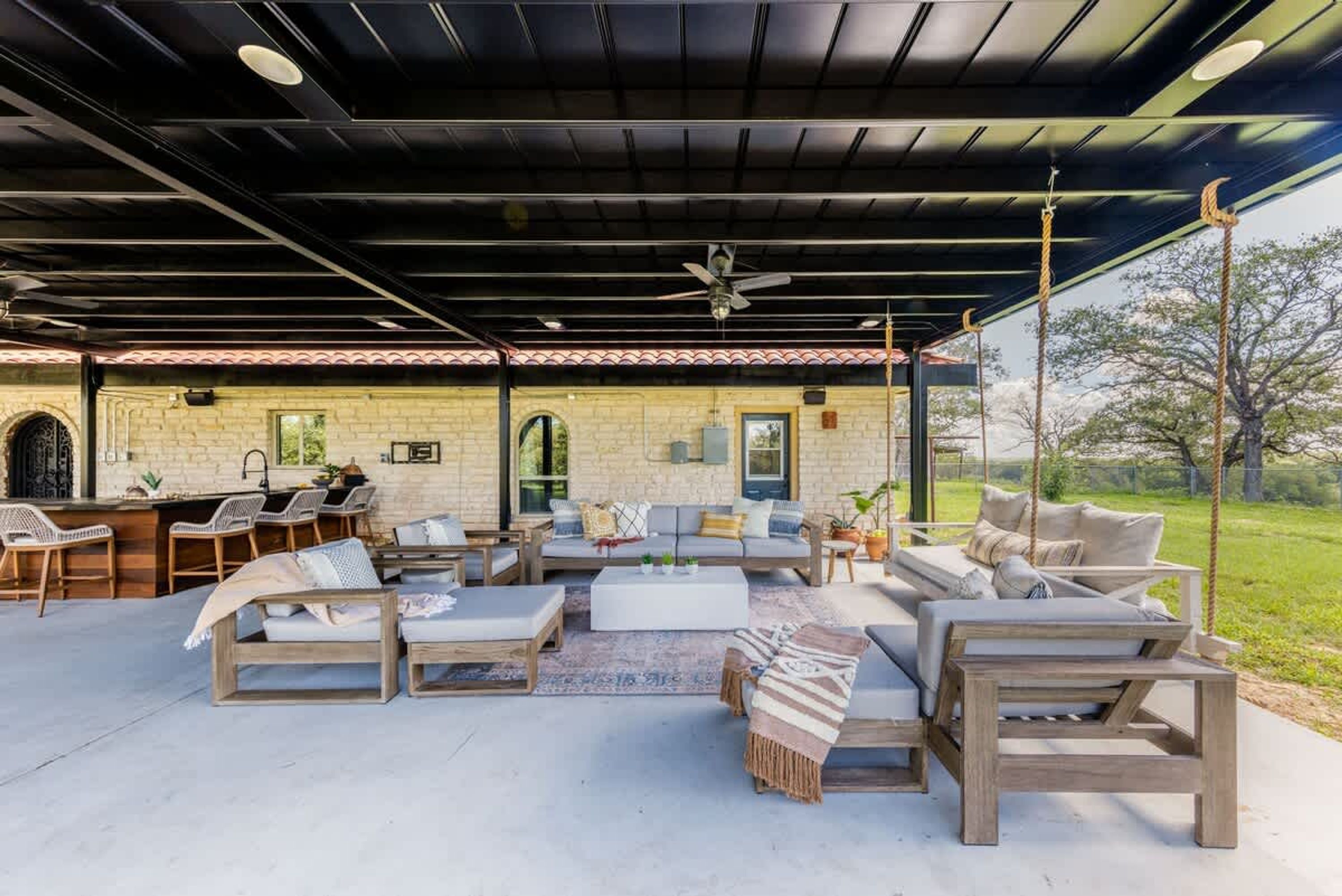An outdoor patio with a stone wall, wooden furniture, and a hanging swing.