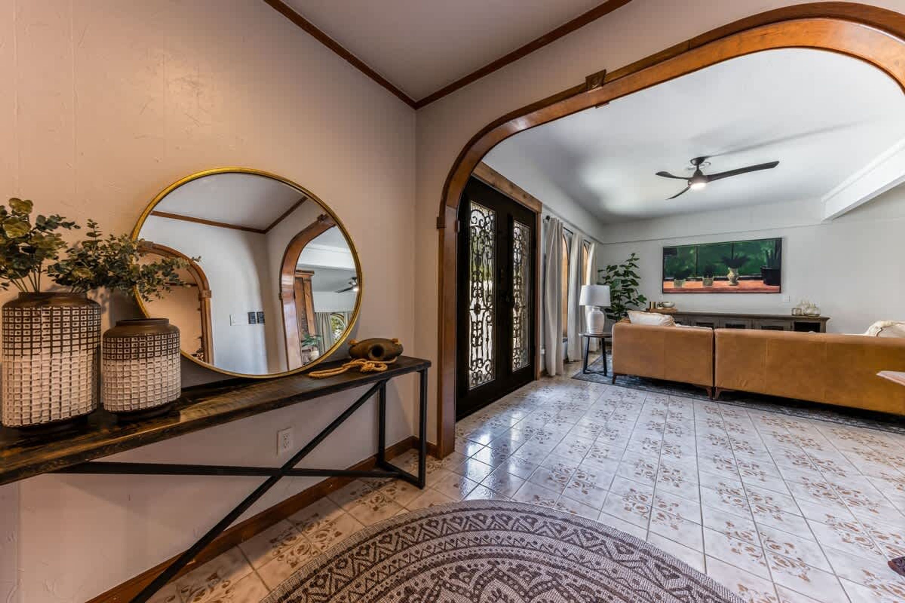 A spacious living area with a large mirror, a console table with decorative vases, a patterned rug, and a sofa.