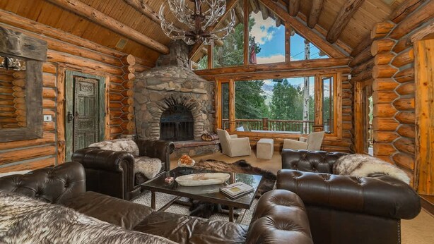 A log cabin interior with a stone fireplace, leather furniture, and large windows offering a view of the outdoors. - Absolutely Amazing Slopeside Mountain Lodge With spa (Telluride)