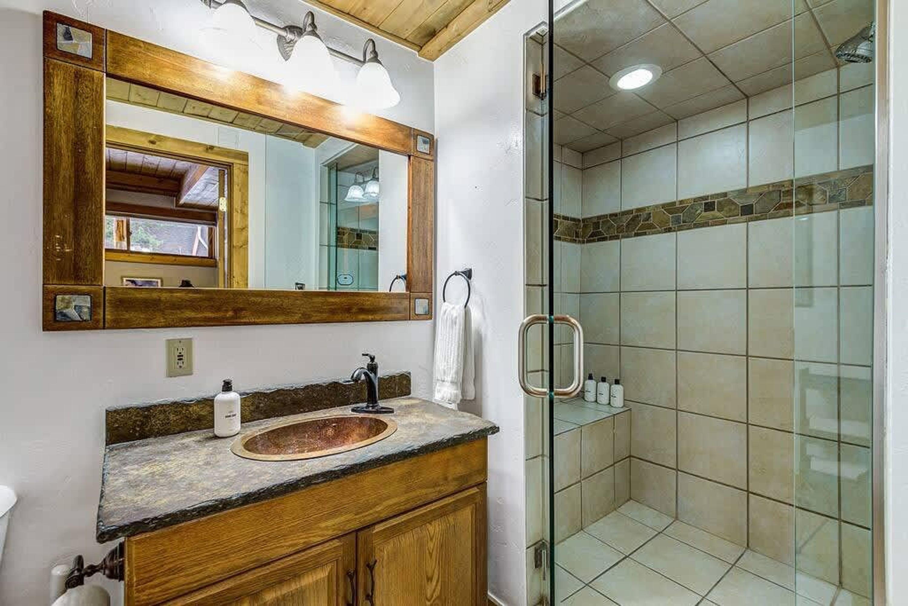 A bathroom with a wooden vanity, a large mirror, a sink, and a glass-enclosed shower.