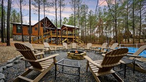 Une cabane dotée d’une terrasse, entourée de fauteuils Adirondack et d’un foyer, avec une piscine en arrière-plan.
