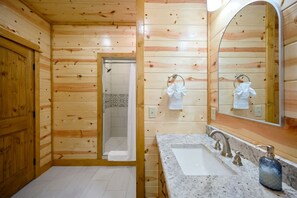 Een houten badkamer in een chalet, met een wastafel, spiegel en douche.