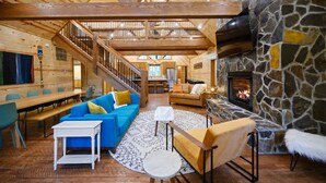 Un intérieur spacieux en bois, agrémenté d’une cheminée en pierre, d’un escalier et d’un coin salon confortable.