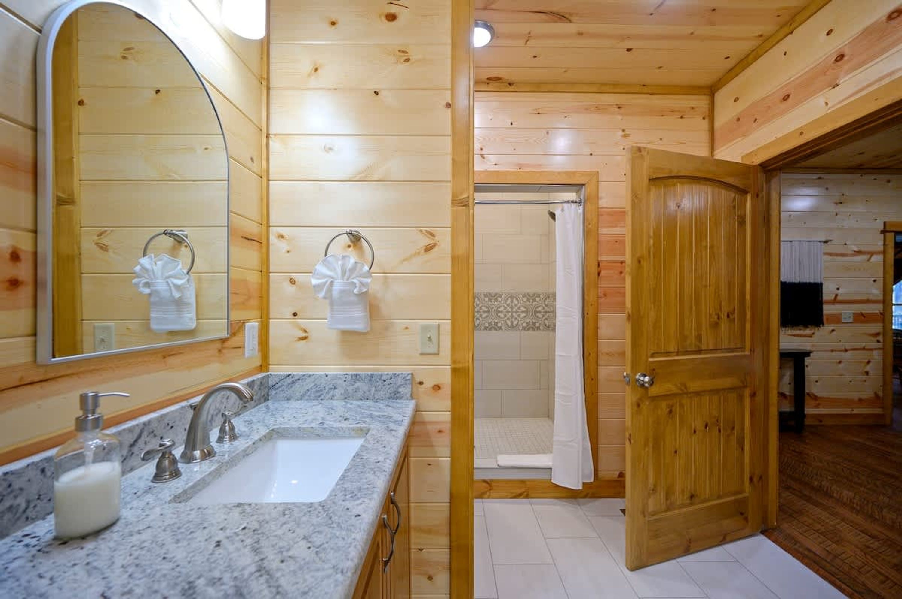 Een houten badkamer met een wastafel, spiegel en douche.