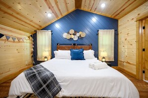 Cozy cabin-style bedroom with a large bed, bedside tables, and a decorative wall hanging.