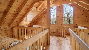 Una cabaña de madera con techo inclinado, un balcón con barandilla y una ventana que ofrece vistas a árboles.