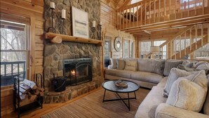 Interior acogedor de una cabaña con chimenea de piedra, vigas de madera, un sofá y una escalera.