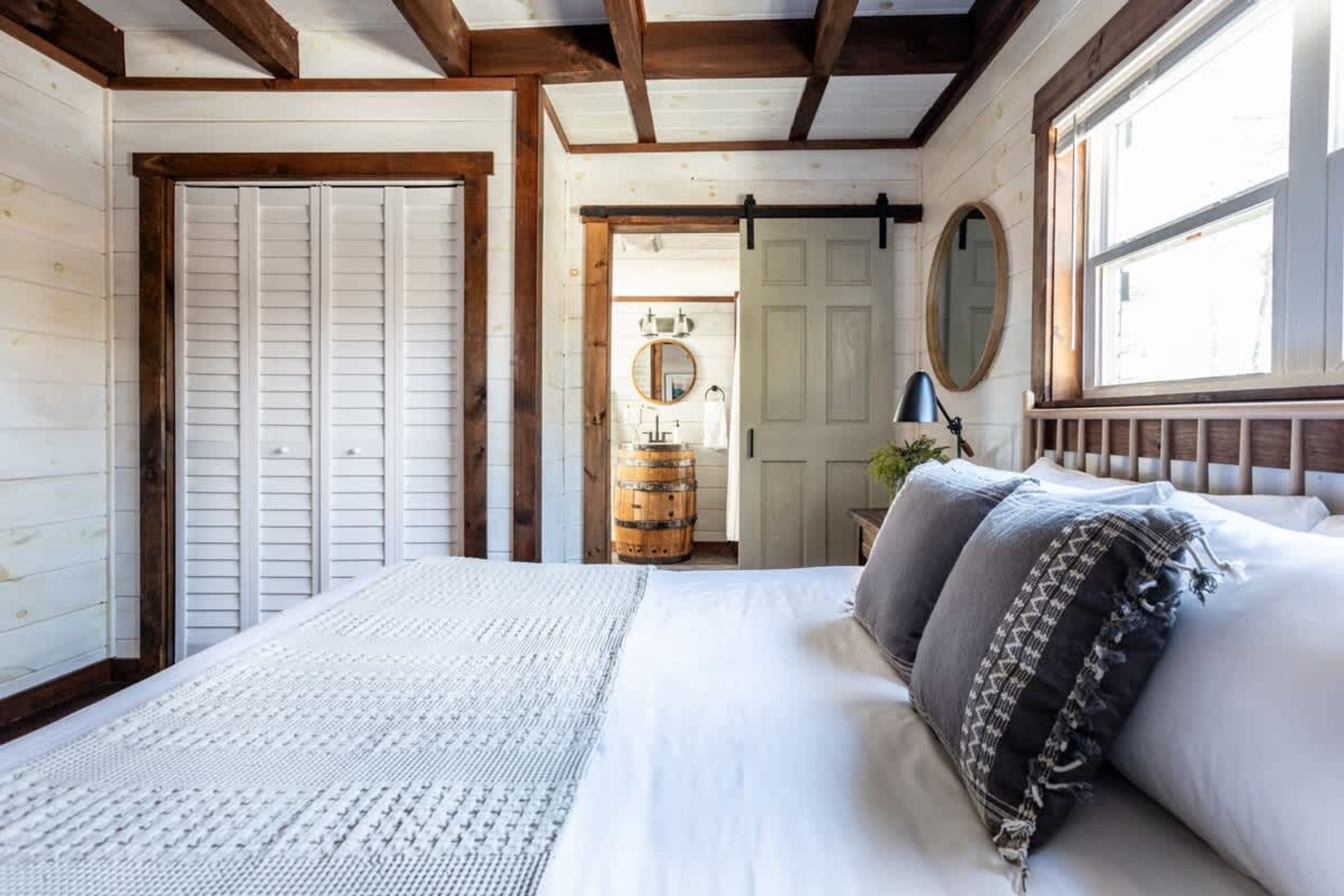 A bedroom with a large bed, a wooden barrel, a mirror, and a window with a view.