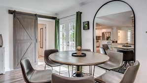 Un espace repas comprenant une table ronde, quatre chaises, une porte coulissante de style rustique et un grand miroir.