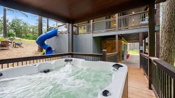 A hot tub with a blue slide, a wooden deck, and a two-story building with balconies.