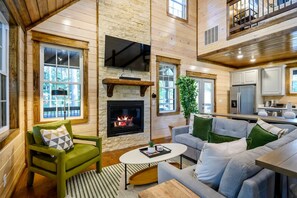Amplia sala de estar con chimenea, televisor y área de cocina con electrodomésticos modernos.