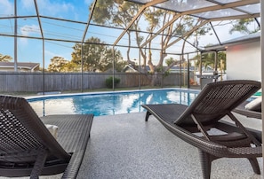 A covered outdoor swimming pool with lounge chairs and a barbecue grill.
