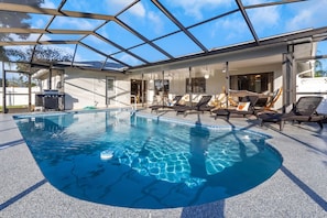 A modern indoor pool with clear blue water, surrounded by lounge chairs and a glass ceiling.