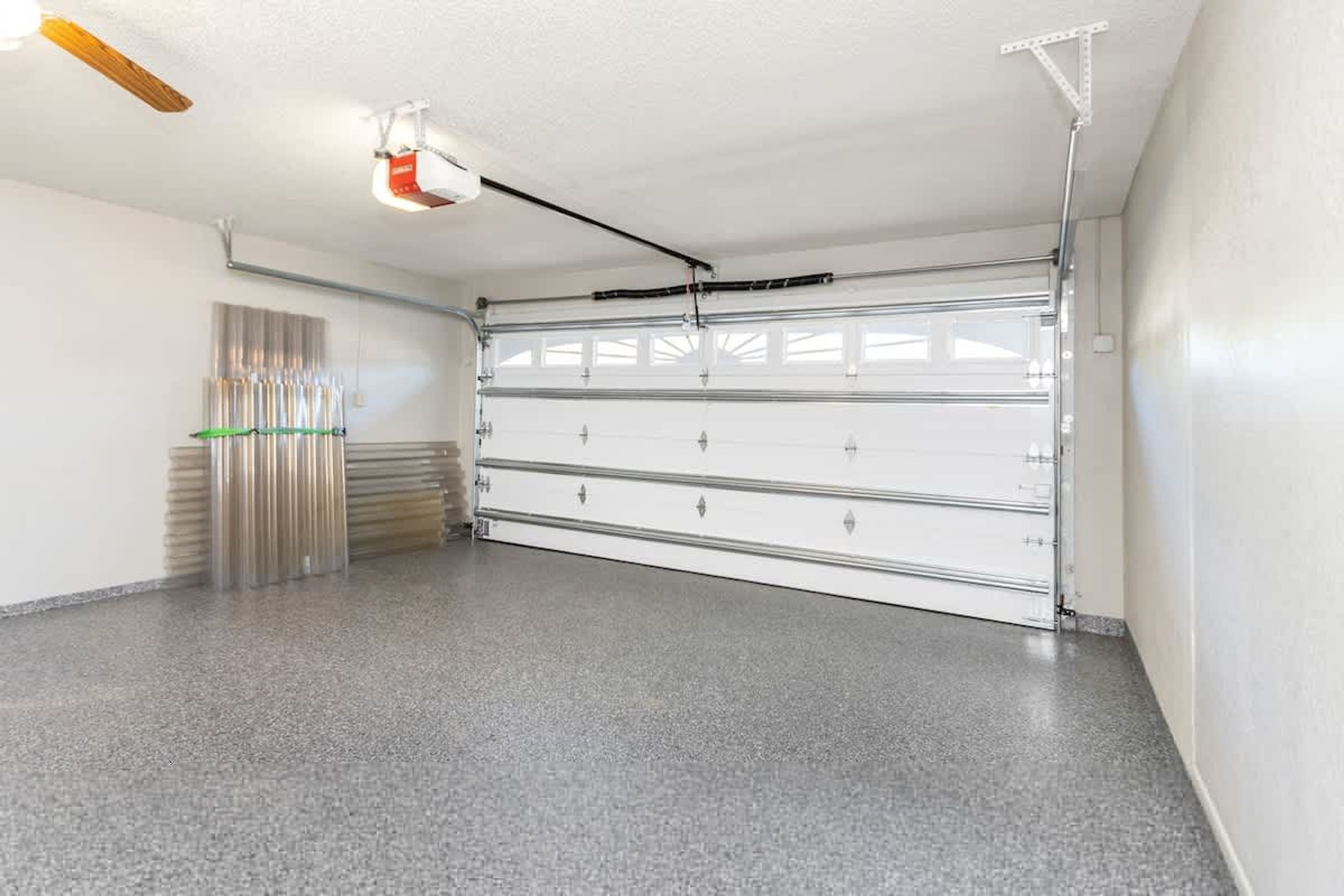 A garage with a closed garage door, a ceiling fan, and a fluorescent light fixture.