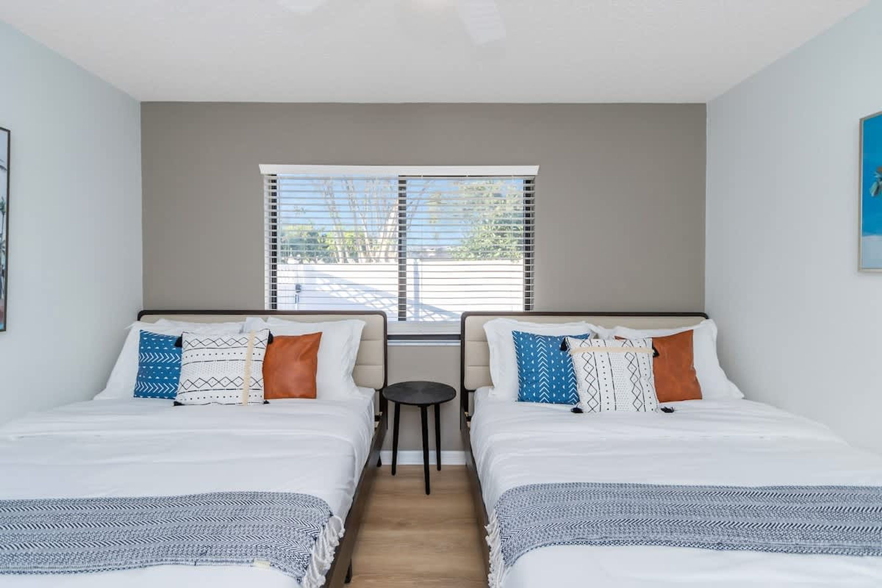 A room with two beds, a small table, and a window with blinds.