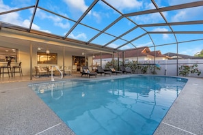 An indoor swimming pool with lounge chairs and a bar area.
