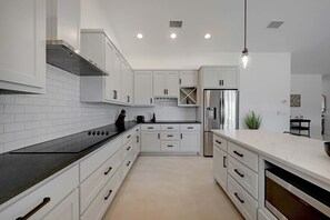 A modern kitchen with white cabinets, black countertops, stainless steel appliances, and recessed ceiling lights. - Secluded Hill Country Getaway Stunning Views Fire Pit 15 Min to Main Street 12 Guests (Fredericksburg)