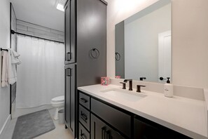 A modern bathroom with a large mirror, two sinks, a toilet, and a shower curtain. - Secluded Hill Country Getaway Stunning Views Fire Pit 15 Min to Main Street 12 Guests (Fredericksburg)