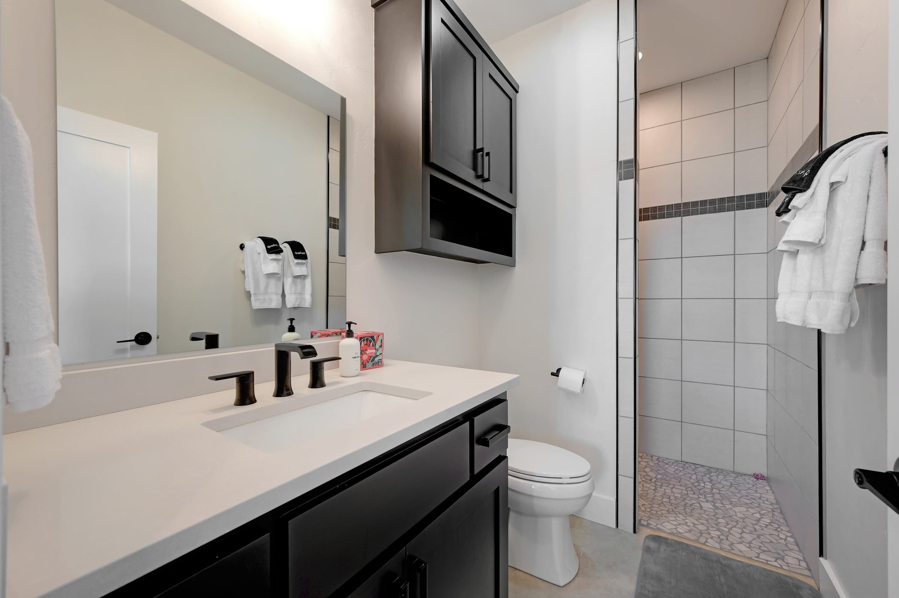 Une salle de bain moderne avec un lavabo blanc, un meuble noir et un espace douche aux murs carrelés.