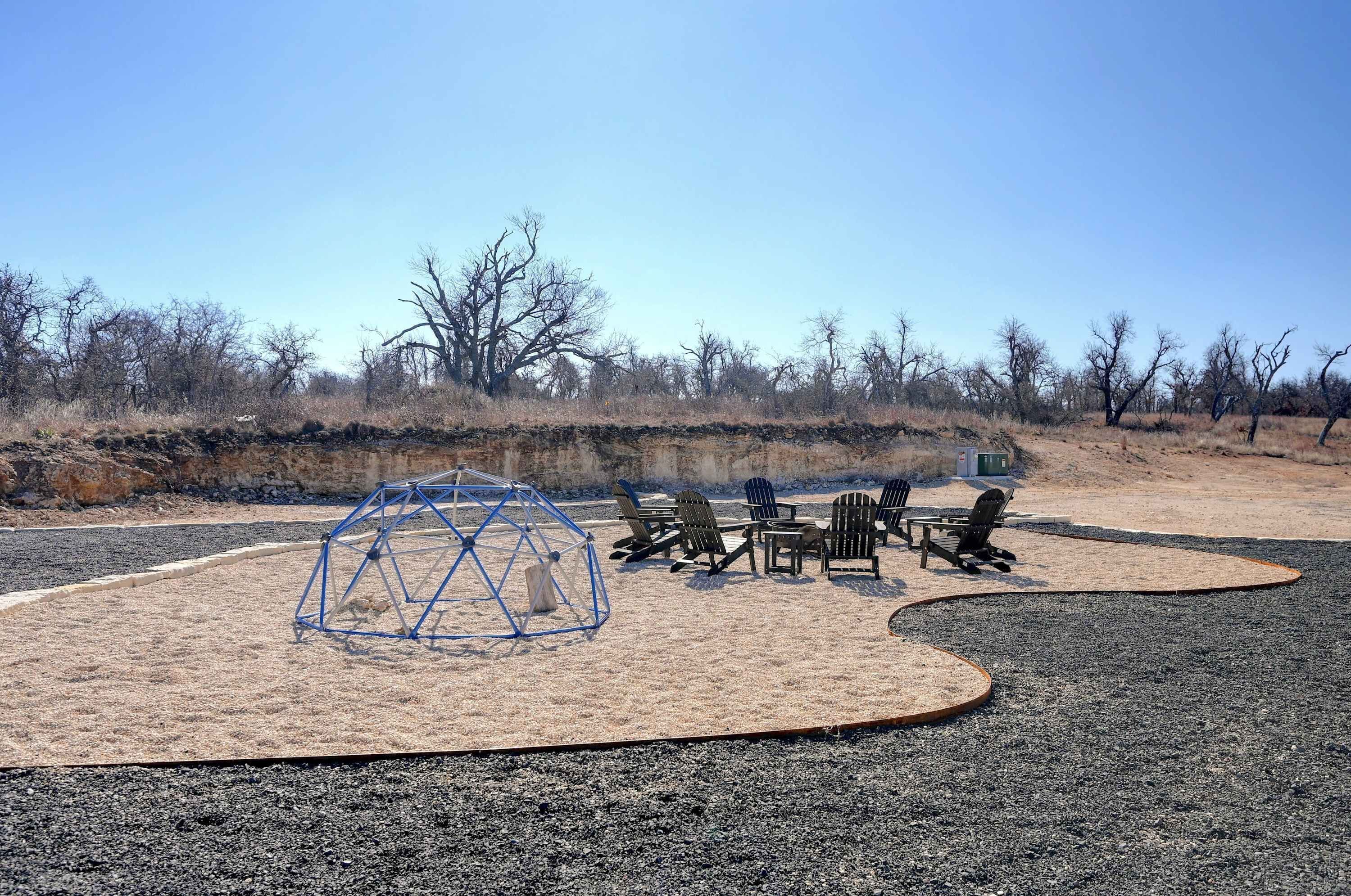 A sandy outdoor area with a blue geodesic structure and several Adirondack chairs.