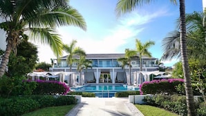 A modern hotel with a swimming pool, surrounded by palm trees and well-maintained gardens. - Luxe Oceanfront Penthouse Hot Tub Daily Cabana (Providenciales)
