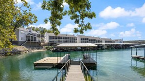 Une propriété située au bord de l’eau, dotée d’un quai menant à une marina, et entourée d’immeubles modernes aux grandes fenêtres.