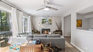 Un salon moderne avec un canapé gris, une cheminée et un ventilateur de plafond.