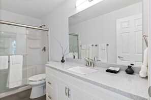 Een moderne badkamer met een douchecabine van glas, een wit toilet, een wastafelmeubel met dubbele wastafel en een grote spiegel.