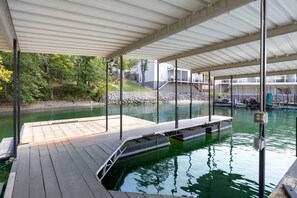 Een overdekte steiger met een houten platform dat over het water uitsteekt, omringd door bomen en gebouwen.