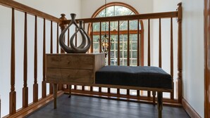 A room with a wooden bench, a wooden chest of drawers, and a large window with a view of greenery.