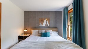 A neatly made bed with white linens and a blue accent pillow, a bedside lamp, and a wall-mounted abstract art piece.