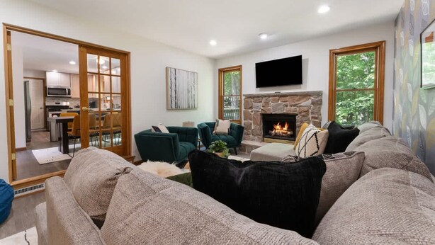A spacious living room with a fireplace, a television mounted above it, and a dining area visible through a glass door.