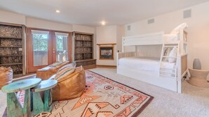 Una habitación acogedora con una cama litera, una chimenea, una estantería y una alfombra estampada.